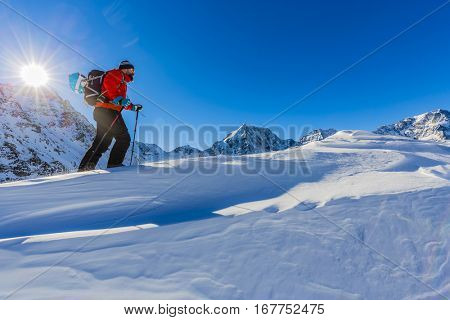 Hiker in winter mountains snowshoeing climbing to the top in sunny cold day in Alps, Italy.