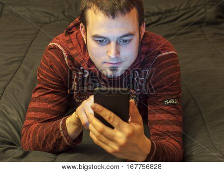 A young man lying on his bed with a cellphone in his hands
