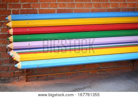 Street bench made from big multicolor pencils near brick wall on street