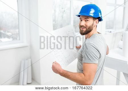 Handsome repairman or builder in helmet working with drawings on renovation of interior