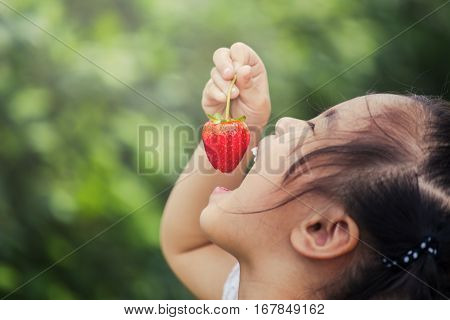 Beautiful little smiling girl eating strawberries in garden