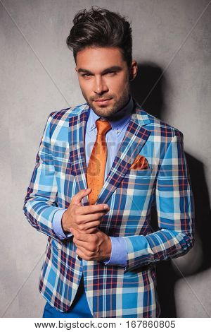 young sexy man in checkered suit stainding with palms together and smiles to the camera in studio
