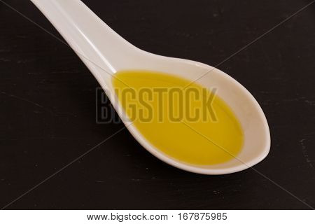 Olive oil presented in a ceramic spoon with a slate background macro.