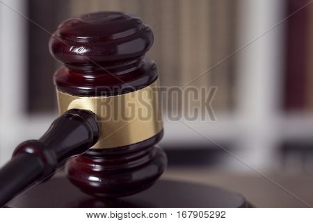 Close up of a judge gavel and law books in the background of a courtroom. Selective focus