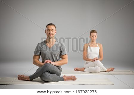 Young athletic man and woman sitting in Gomukhasana Cow face pose on yoga mats