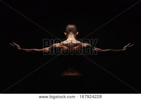 Unrecognizable man bodybuilder shows strong hands and neck muscles, athletic trapezius. Low key, studio shot on black background.