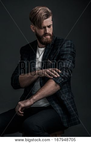 Used to look perfect. Stylishly dressed young man adjusting his jacket while sitting against grey background