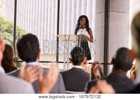 Audience at seminar applauding young black woman at lectern