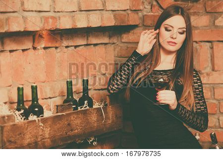 Elegant beauty lady long hair full make up wearing black dress tasting wine in rural cottage interior celler