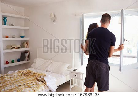 Couple by window in bedroom, back view three quarter length
