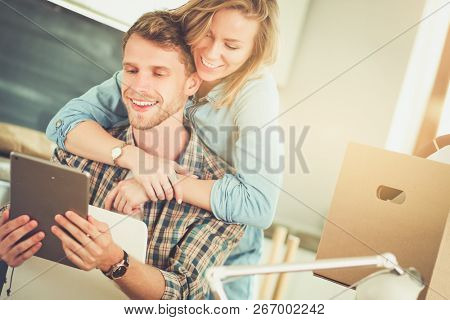 Young couple moving in new home.Sitting and relaxing after unpacking.Looking something on laptop. Young couple