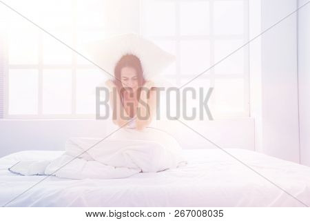 Young caucasian woman covering her head and ears with pillows.