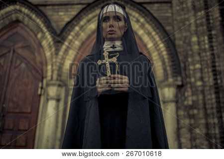 Beautiful Young Nun In Black Cassock, Cloak And Transparent Cape Is Standing And Praying With Cross 