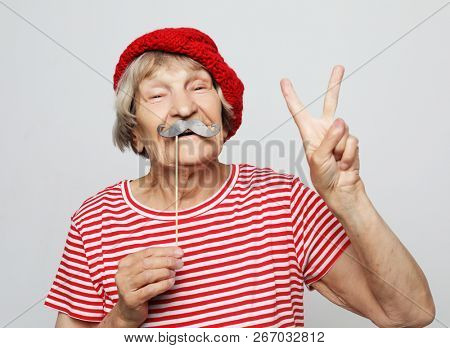 lifestyle, people and party concept: funny grandmother wearing red clothes holding falce glasses