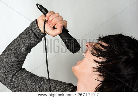 The Young Black Hair Guy Is Singing Or Screaming In The Microphone On Gray Background.