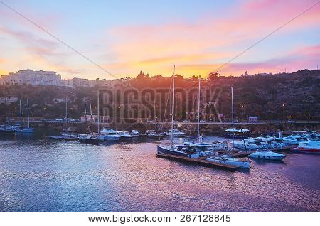 The Bright Sunset Sky Over The Yacht Haven With Moored Boats And Rocky Hills On Background, Ghajnsie
