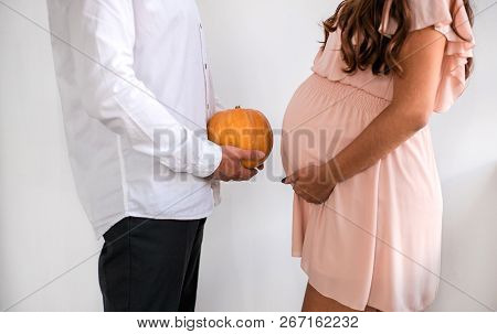 Man With Pumpkin Is Standing Opposite A Pregnant Woman. Happy Halloween Concept.