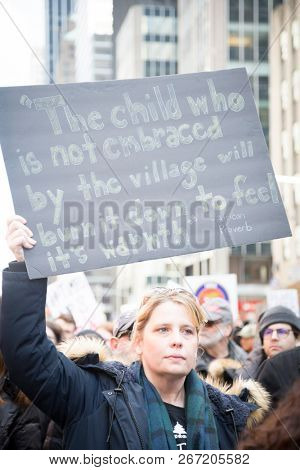 March For Our Lives: A woman in the march to end gun violence holds a sign with a quote from an African proverb referencing children who are not embraced by the village, 6th Ave, NEW YORK MAR 24 2018.