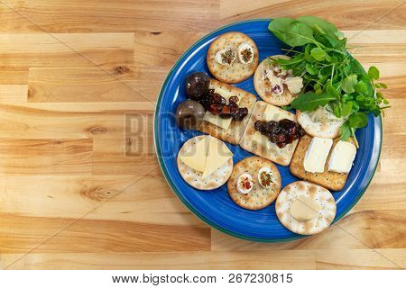 Crackers Topped With A Selection Of Cheeses, With Pickles And Salad Leaves. On A Blue Plate On A Woo