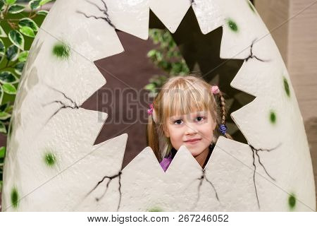 Cute Baby Girl In Artificial Cracked Dinosaurus Egg. Little Kid Smiling And Having Fun At Indoor Pla