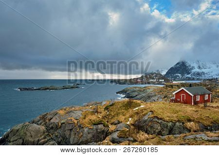 Clif with traditional red rorbu house on Litl-Toppoya islet on Lofoten Islands, Norway in winter