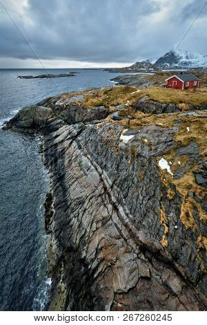 Clif with traditional red rorbu house on Litl-Toppoya islet on Lofoten Islands, Norway in winter