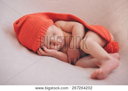 A Naked Newborn Baby Sleeps In A Christmas Hat.