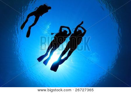 Underwater Image of Scuba Divers silhouetted against sun. Two Students practice skills under the supervision of Diving Instructor
