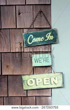 Old, Weathered Wood Hanging Signs On Shingled Exterior Of Building Advertising That The Shop Is Open