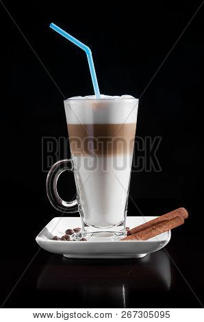 Latte Macchiato In A Glass With White Plate, Spoon, Decorated With Coffee Beans, Cinnamon On Black B
