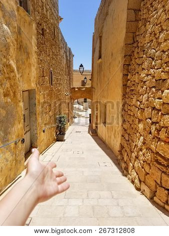 Girl Makes A Welcome Guesture On Old Narrow Beautiful Street With Narrow Walls Of Victoria, Malta In