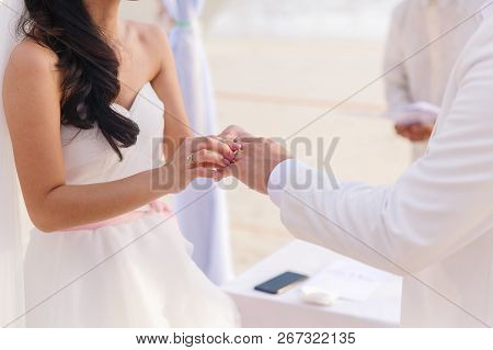 Bride Giving An Engagement Ring To Her Groom Under The Arch Decorated With Flowers On The Sandy Beac