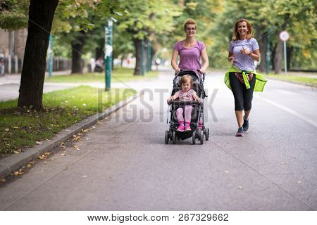two young healthy women jogging together while pushing a baby stroller at city park