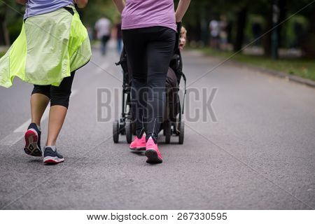 two young healthy women jogging together while pushing a baby stroller at city park