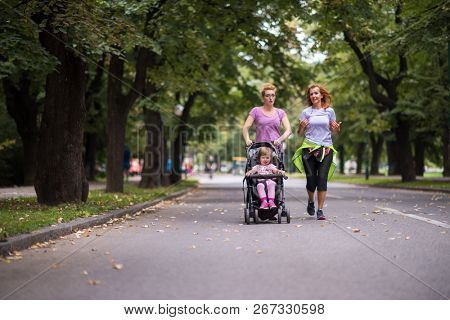 two young healthy women jogging together while pushing a baby stroller at city park