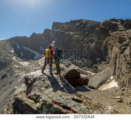 Two Anonymous Travelers Standing On Rough Rock And Admiring Picturesque View Of Majestic Mountains I