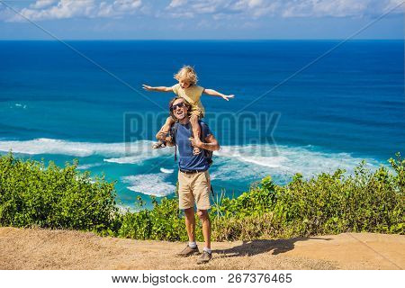 Dad And Son Travelers On A Cliff Above The Beach. Empty Paradise Beach, Blue Sea Waves In Bali Islan