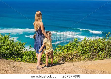 Mom And Son Travelers On A Cliff Above The Beach. Empty Paradise Beach, Blue Sea Waves In Bali Islan
