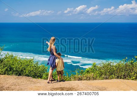 Mom And Son Travelers On A Cliff Above The Beach. Empty Paradise Beach, Blue Sea Waves In Bali Islan