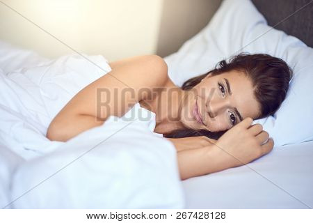 Young Beautiful Latin Woman Woman With Long Brunette Hair Lying In Her Bed With White Sheets Smiling