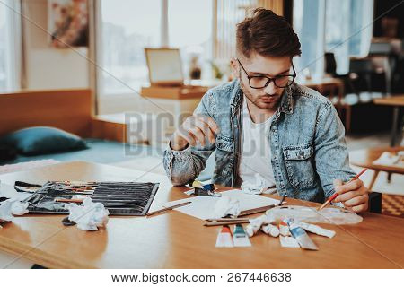Young Male Talanted Artist Focused On Paining. Closeup Portrait Of Handsome Painter Sitting At Woode
