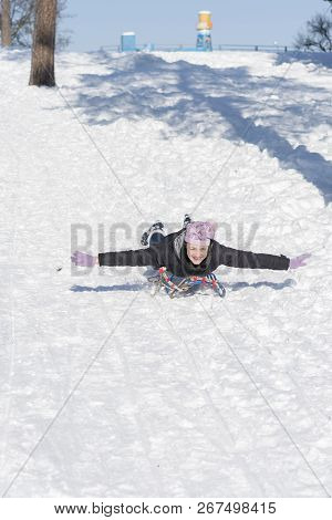 Young Woman Sledding In Snow. Laughing Girl In Winter Clothing Goes Down On Sleds Down The Hill. Ert