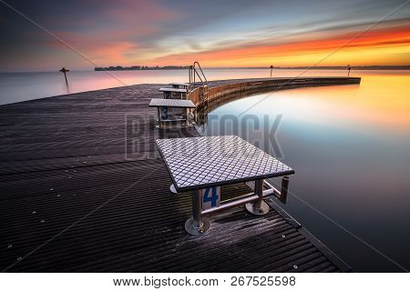 Beautiful Morning At The Lake On A Long Jetty With Wooden Planks, Morning Dew And A Colorful Sunrise
