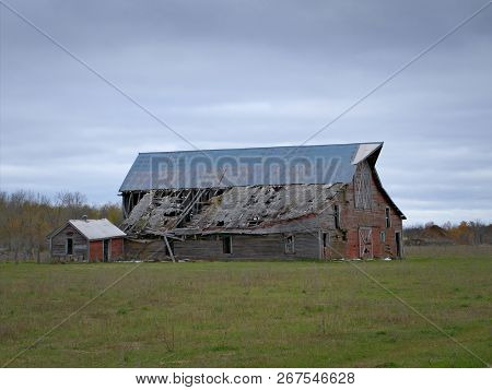 Drab Abandoned Dilapidated Farm Barn And Shed With Clouds In Northern Minnesota