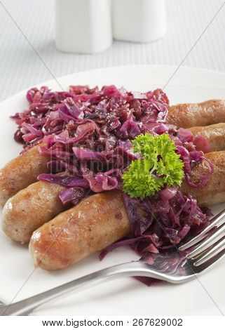 German Thuringer Sausage Or Bratwurst, With Spiced Red Cabbage With Apple, On A Plate With A Fork.