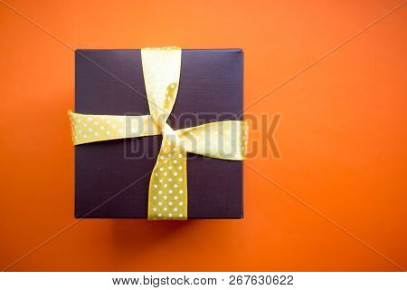 Brown Gift Box With Yellow Ribbon On Orange Background. Top View With Copy Space.