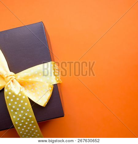 Brown Gift Box With Yellow Ribbon On Orange Background. Top View With Copy Space.