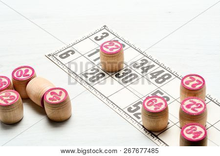Board Game Lotto Or Bingo. Some Wooden Lotto Barrels With Numbers And One Card On White Table During