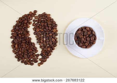 Roasted Brown Coffee Beans Laid Forming A Shape Of A Big Coffee Bean Next To Beautiful White Porcela