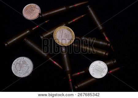One Euro, One Russian Ruble And Ukrainian Hryvna Coins With Rifle Military Ammo On Black Background.